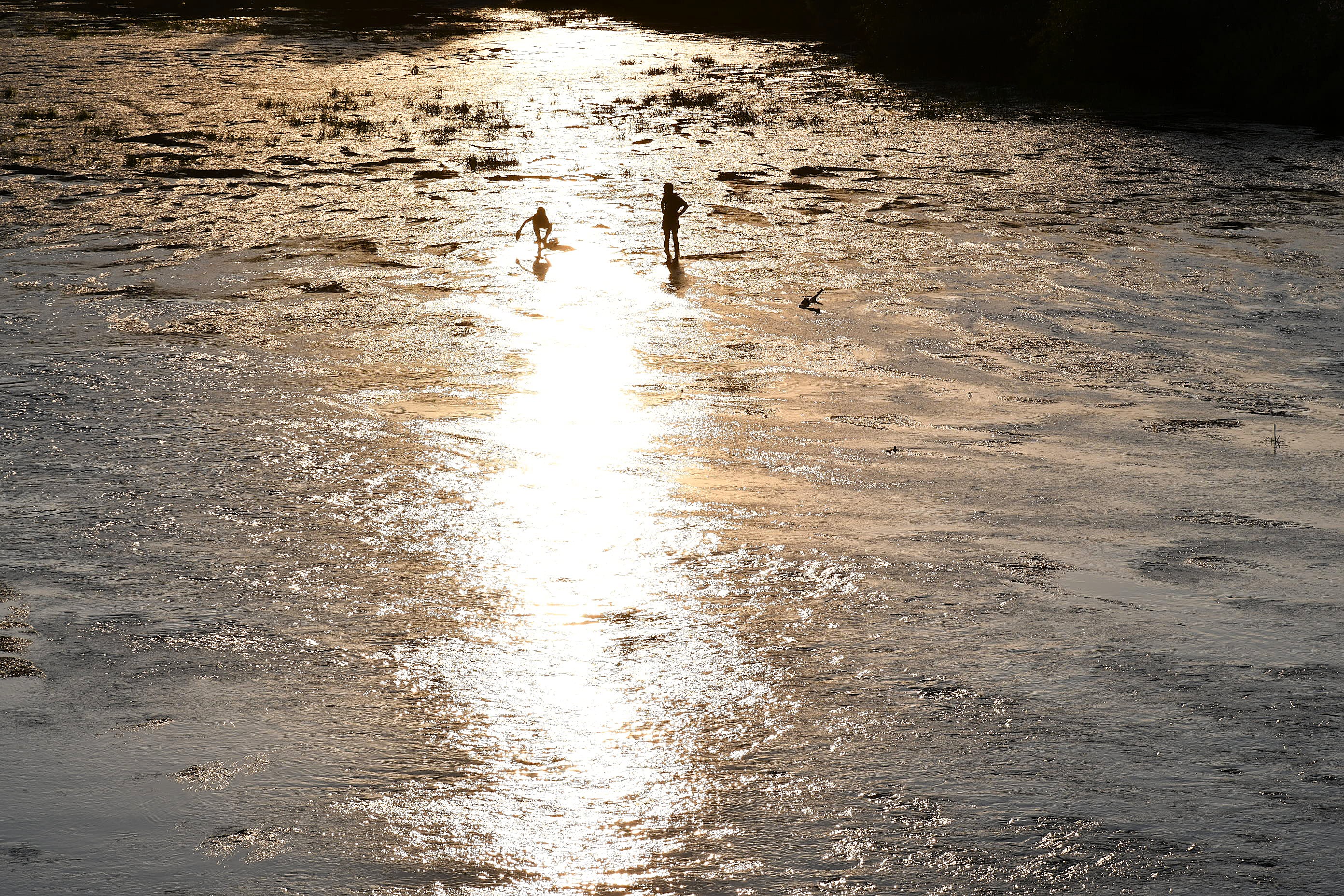 Zwei Kinder spielen im flachen Wasser der Fulda im Gegenlicht der Abendsonne